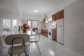 A kitchen with a dining table, chairs, a washing machine, and cabinets.