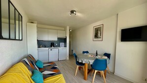 A compact living space with a sofa, a dining table with chairs, a kitchenette, and a flat-screen TV mounted on the wall. - DES AILES - Apartment Port Haliguen - parking - 1bedroom (Quiberon)