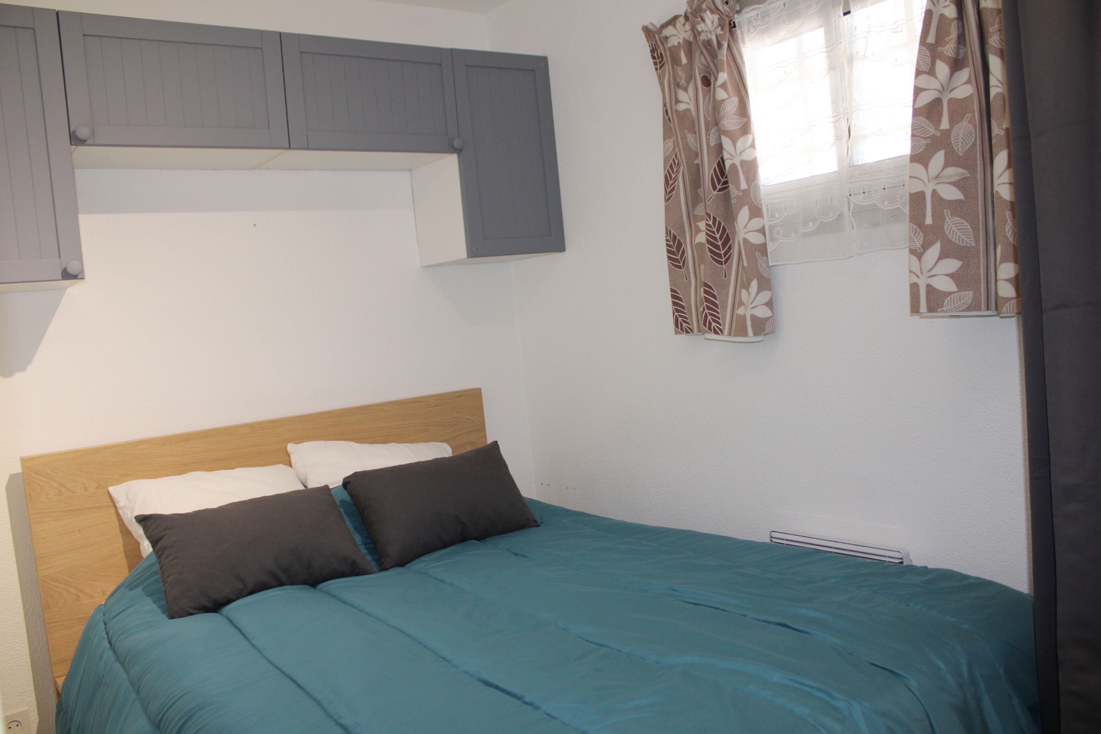 Une chambre à coucher comprenant un lit, une tête de lit, une fenêtre avec des rideaux et un meuble fixé au mur.