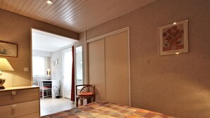 A bedroom with a bed, a chair, a desk, and a door leading to another room.