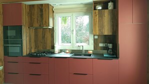 A kitchen with wooden cabinets, a built-in oven, a window with a view of greenery, and a coffee maker on the countertop.