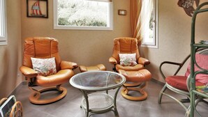 A room with two leather recliner chairs, a small glass table, and a metal chair with a red cushion.