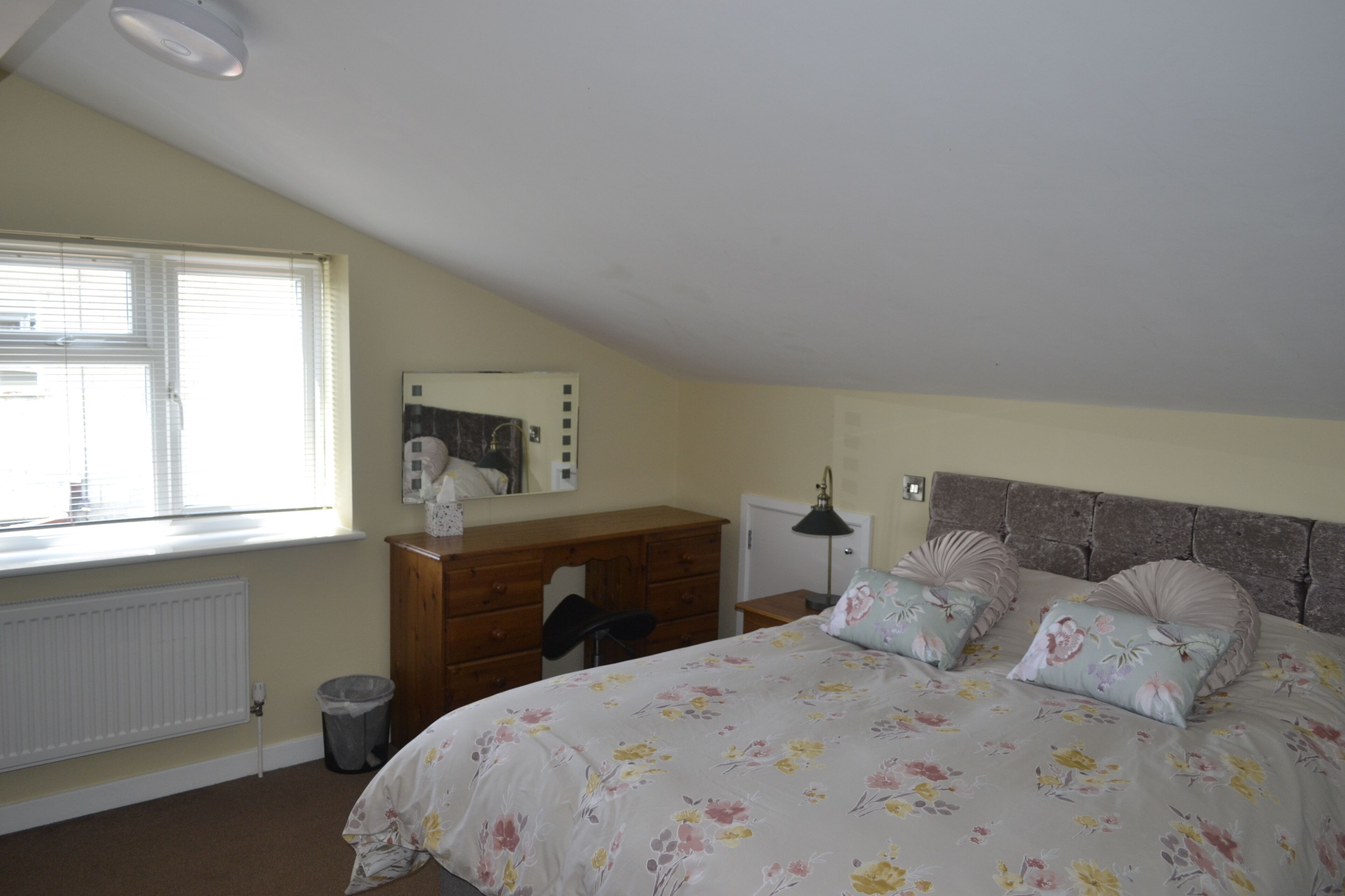 A bedroom with a bed, dresser, desk, and radiator.