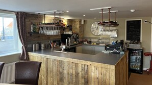 Una zona de bar con mostrador de madera, vasos colgantes y un reloj en la pared.