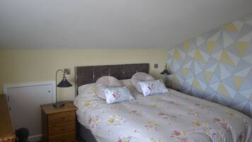 Une chambre à coucher comprenant un lit, deux lampes de chevet, une table de chevet en bois avec des tiroirs, un bureau et un mur décoré d’un motif.