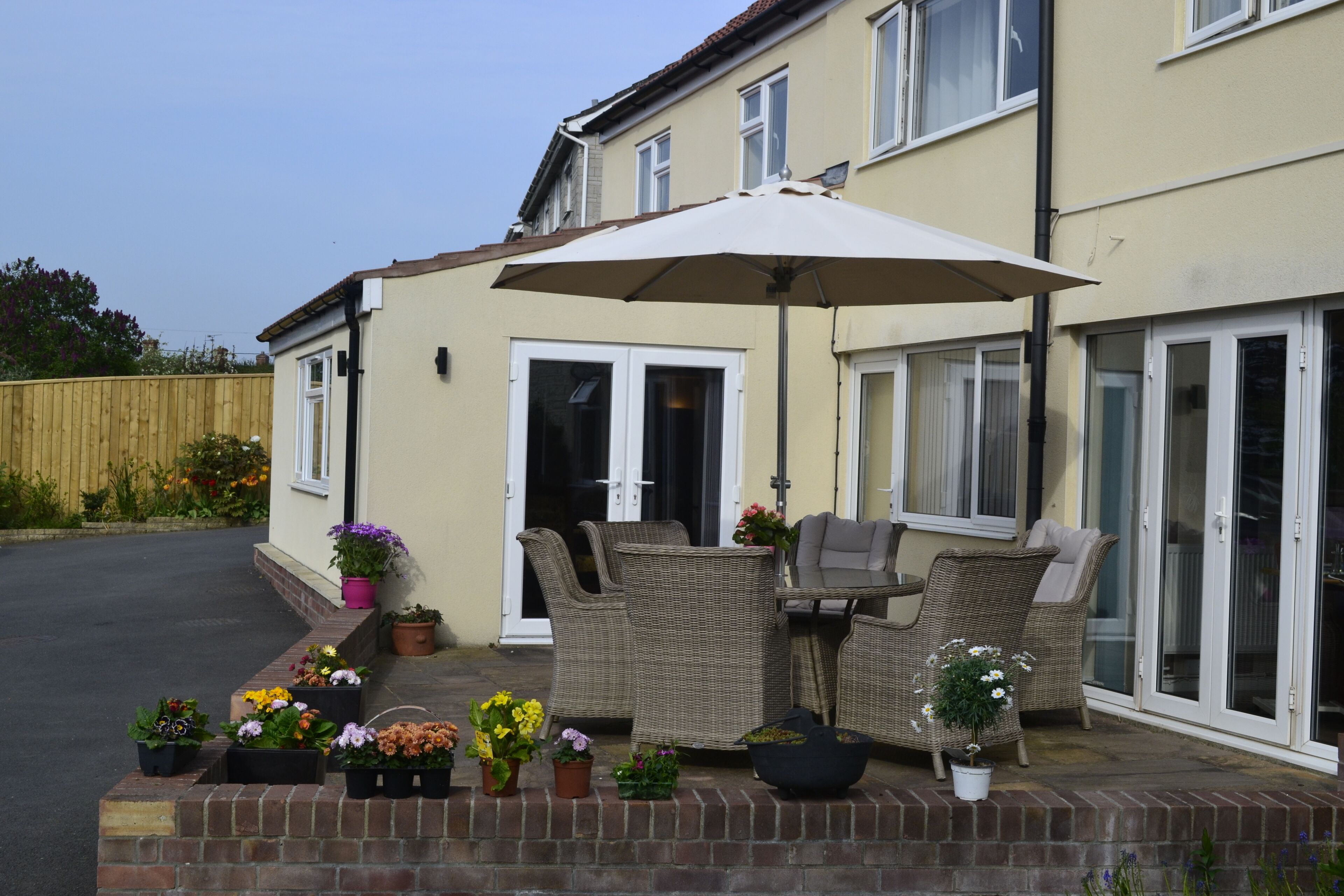 A patio with wicker furniture, a table, and an umbrella. There are potted plants and a brick wall.