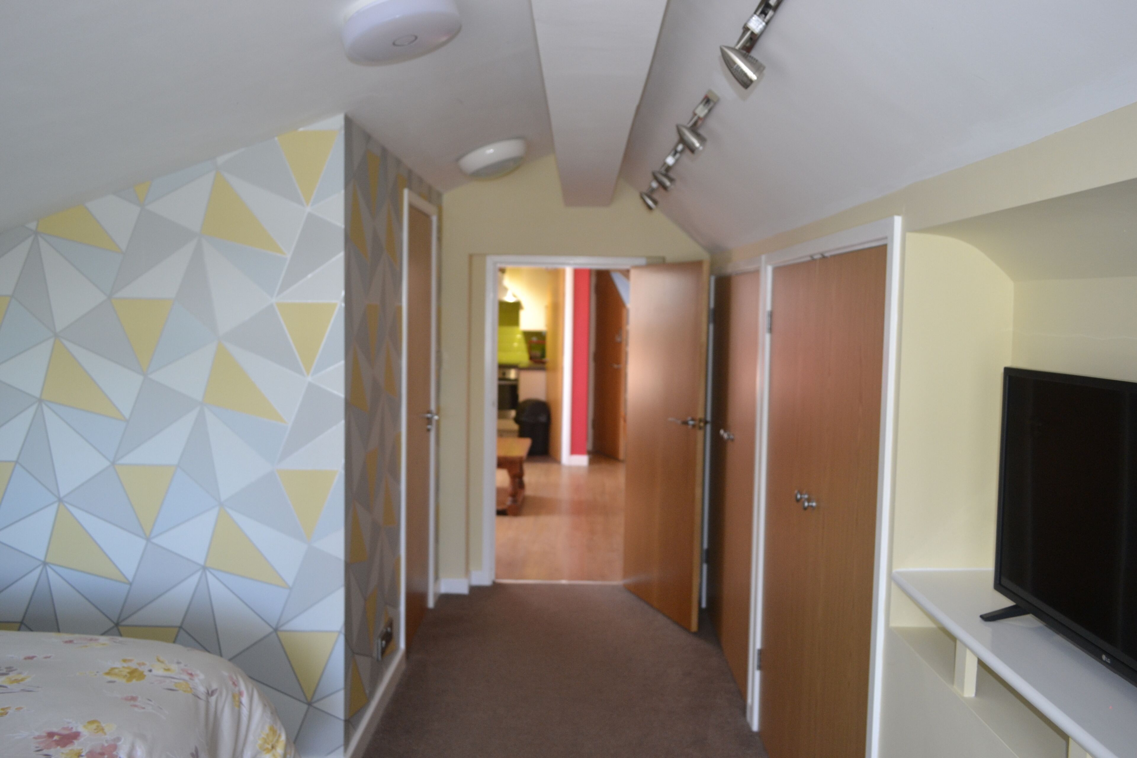 A hotel room with a bed, a TV on a stand, a wardrobe, and a hallway leading to another room.