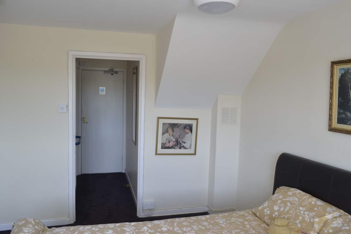 A bedroom with a bed, a door leading to another room, a framed picture on the wall, and a ceiling light.