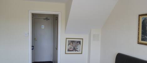 A bedroom with a bed, a door leading to another room, a framed picture on the wall, and a ceiling light.