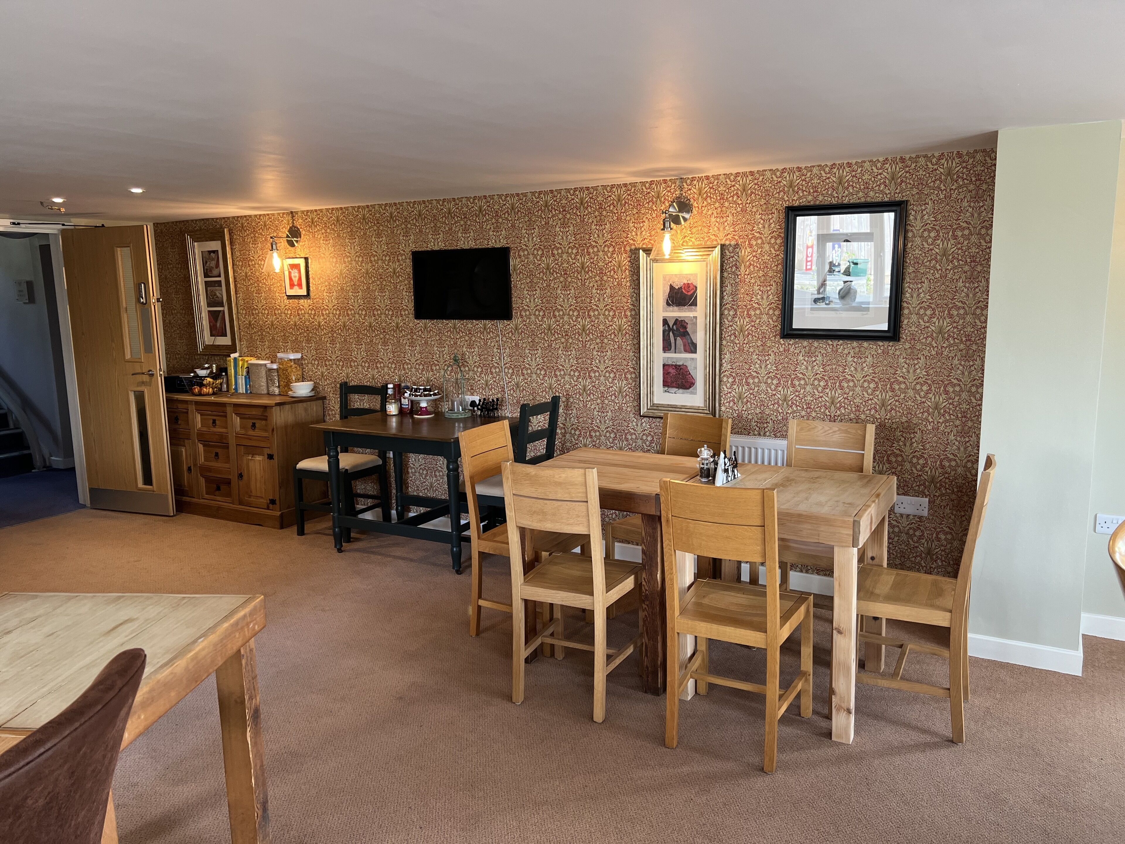 A dining area with a wooden table and chairs, a kitchen area with cabinets and a countertop, and a patterned wallpaper.