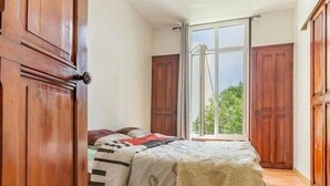 A bedroom with a bed, wooden wardrobe, and a large window with a view of greenery.