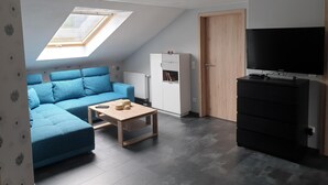 Una sala de estar moderna con un sofá azul, una mesita de madera, un armario blanco, un mueble de TV negro y un tragaluz.