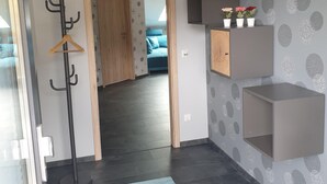 Un pasillo con un perchero, una alfombra azul y una puerta que da a un dormitorio con cama y almohadas azules.