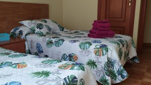 Una habitación con dos camas, cada una con una colcha de motivos florales, cabecero de madera y una pila de toallas moradas en la cama de la derecha.