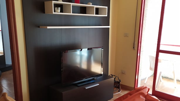 Una sala de estar moderna con un mueble multimedia oscuro, un televisor de pantalla plana, un sillón informal rojo y una mesa de centro de vidrio.