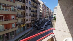 Un edificio residencial de varios pisos con balcones, una calle con coches estacionados y una acera.