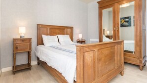 A bedroom with a wooden bed, two bedside tables with lamps, a large mirror, and a wooden wardrobe. - Countryside Cottage with Private Terrace and Garden, Near Châteaubriant (Grand-Auverné)