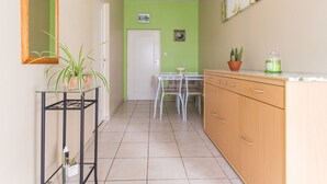 A narrow hallway with a green wall, a white door, a small table with chairs, a wooden cabinet, and a potted plant. - Countryside Cottage with Private Terrace and Garden, Near Châteaubriant (Grand-Auverné)
