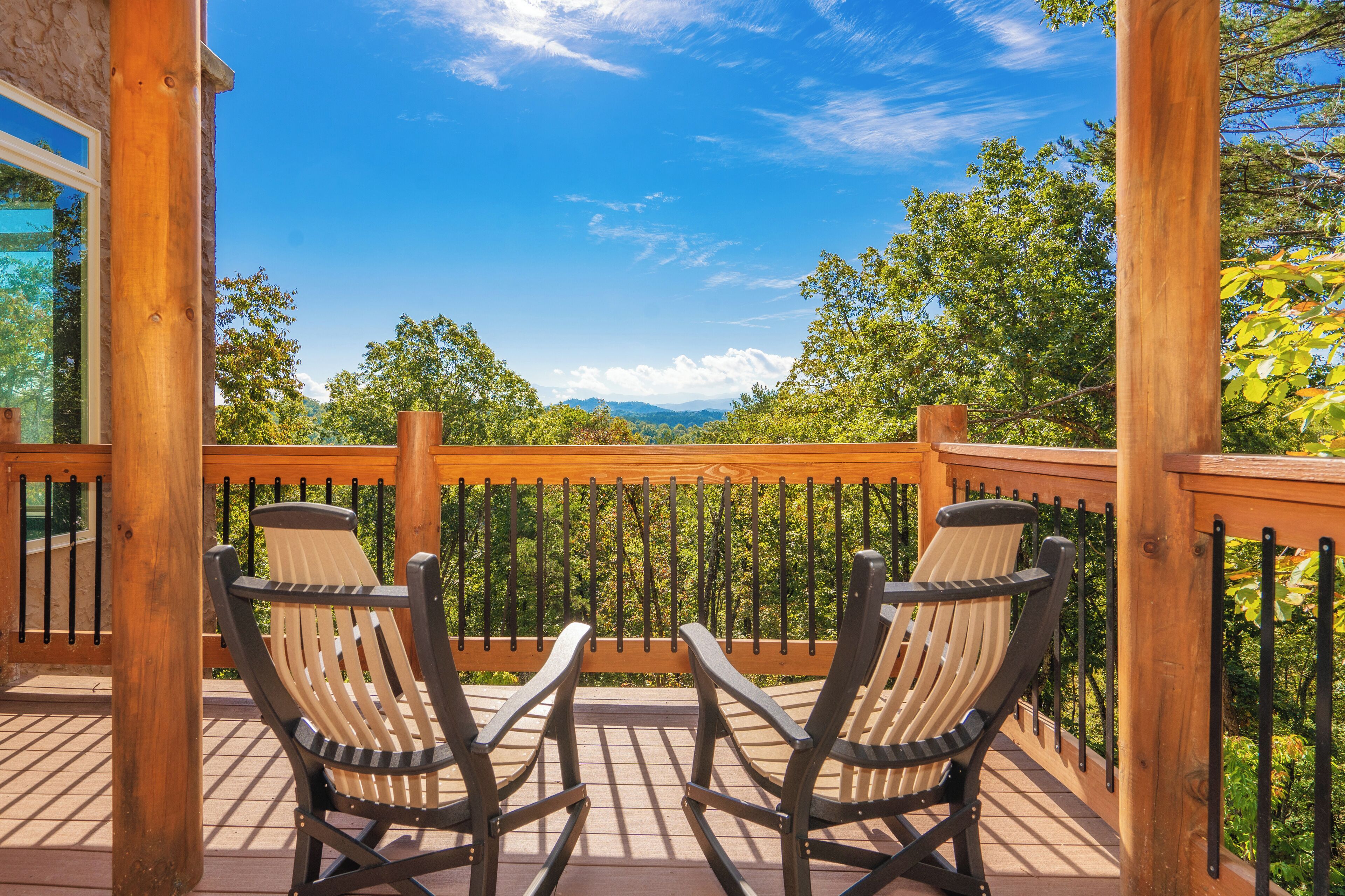A wooden deck with two rocking chairs facing a scenic view of trees and mountains.