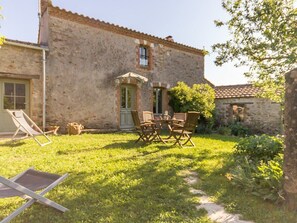 A stone building with a small patio area featuring a table and chairs, a door, and a window. - Charming House in Rouans - Wifi, Pets Allowed (Rouans)