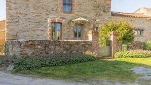 Un bâtiment en pierre avec un toit en tuiles, une petite fenêtre et une porte sur laquelle est apposée une enseigne.