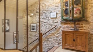 Une pièce avec un mur en pierre, un escalier en bois et un meuble où sont rangés des chapeaux.