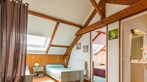 A bedroom with a sloped ceiling, wooden beams, a bed, a nightstand, a lamp, and a window with a curtain. - Charming Cottage with Fireplace, Mezzanine, and Garden near Guérande (Saint-Molf)