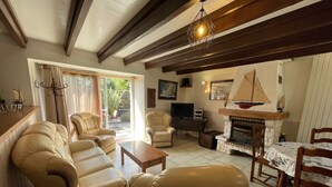 A living room with leather sofas, a TV, a fireplace, and a dining area. - Charming Cottage with Fireplace, Mezzanine, and Garden near Guérande (Saint-Molf)