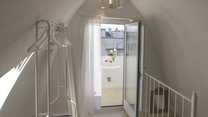 A narrow stairway with a metal handrail, a glass door leading to an outdoor balcony with a table and chairs, and a white curtain partially drawn.