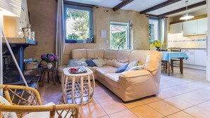 Ein gemütliches Wohnzimmer mit einer Couch, einem kleinen Tisch und einem Korbstuhl. Ein Fenster bietet Blick auf Grünfläche.