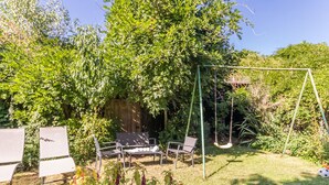 Ein Garten mit Schaukel, zwei Liegestühlen und einem Esstisch.