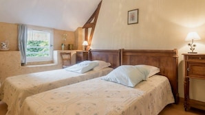 Ein Zimmer mit zwei Betten, einem Fenster mit Blick auf Grünflächen, einem Holzkopfende, einem Nachttisch mit Lampe und einem an der Wand hängenden Bild.