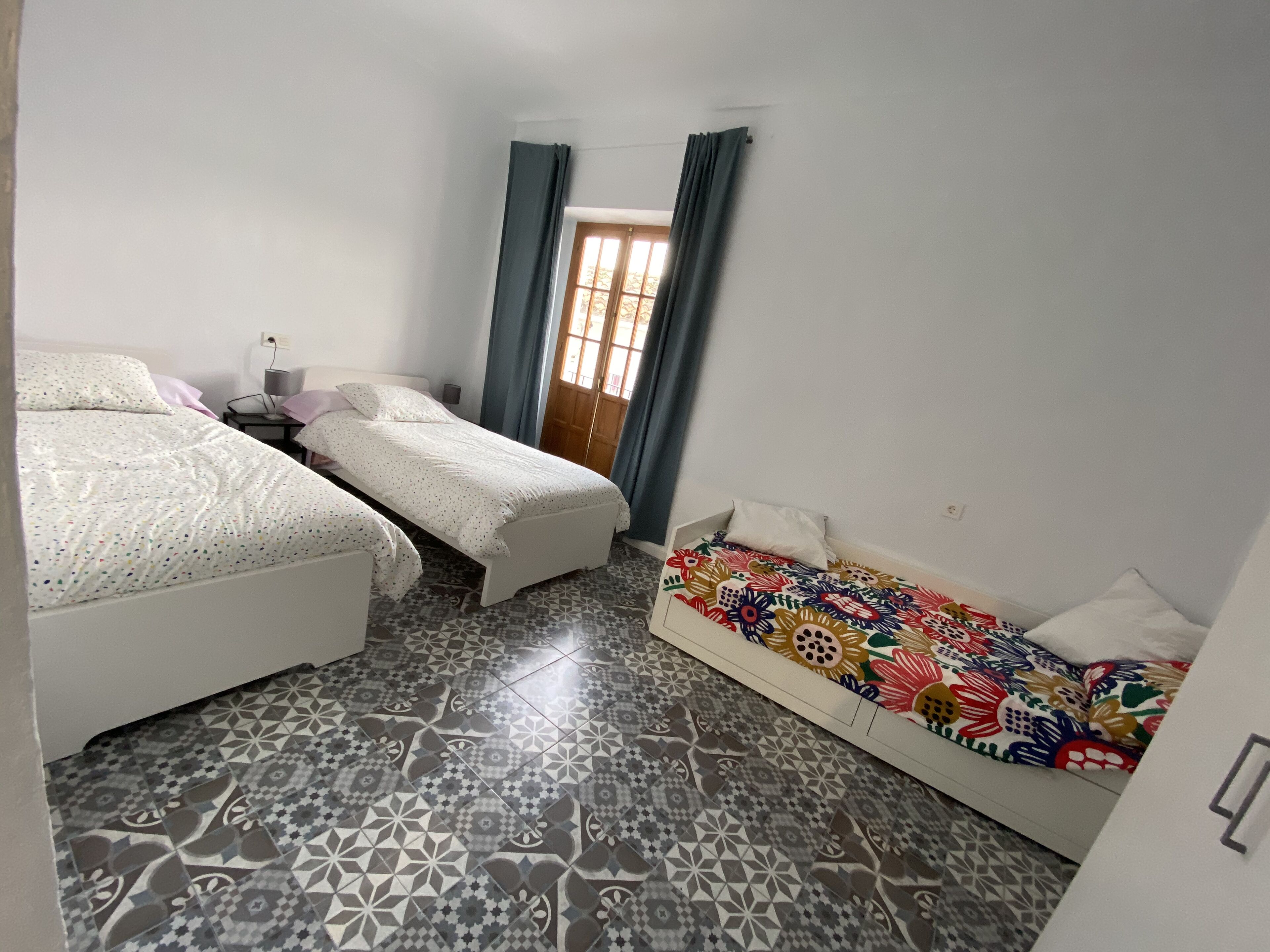 Un dormitorio con dos camas, piso estampado y ventana con cortinas.