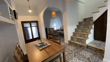 Un comedor con una mesa y sillas de madera, una escalera con baldosas estampadas y una lámpara colgante.