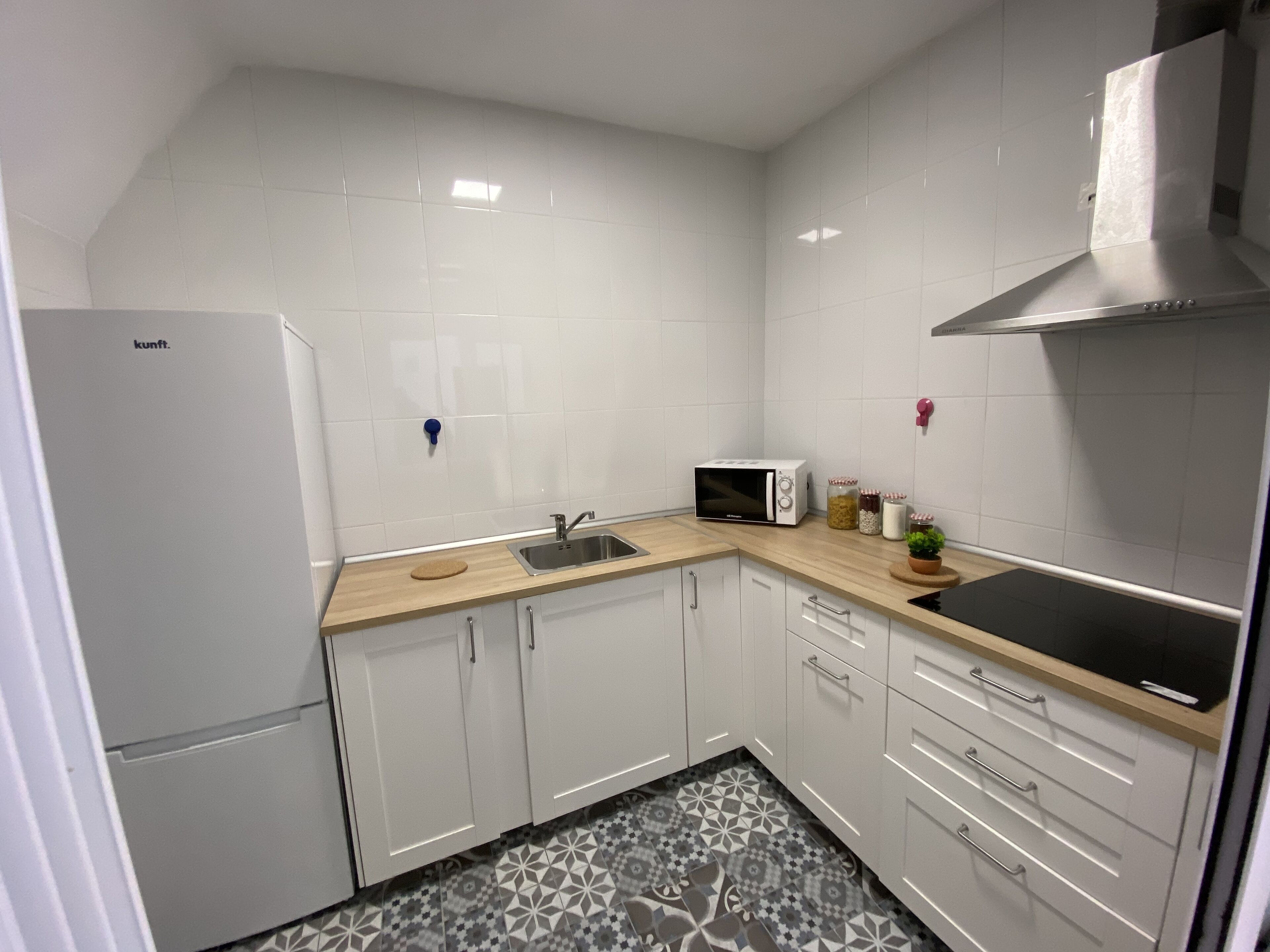 Una cocina compacta con gabinetes blancos, un microondas, un fregadero y una campana extractora de acero inoxidable.