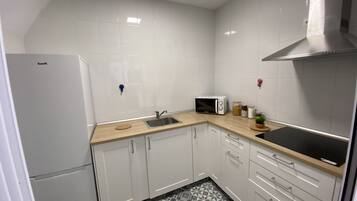 Una cocina compacta con gabinetes blancos, un microondas, un fregadero y una campana extractora de acero inoxidable.