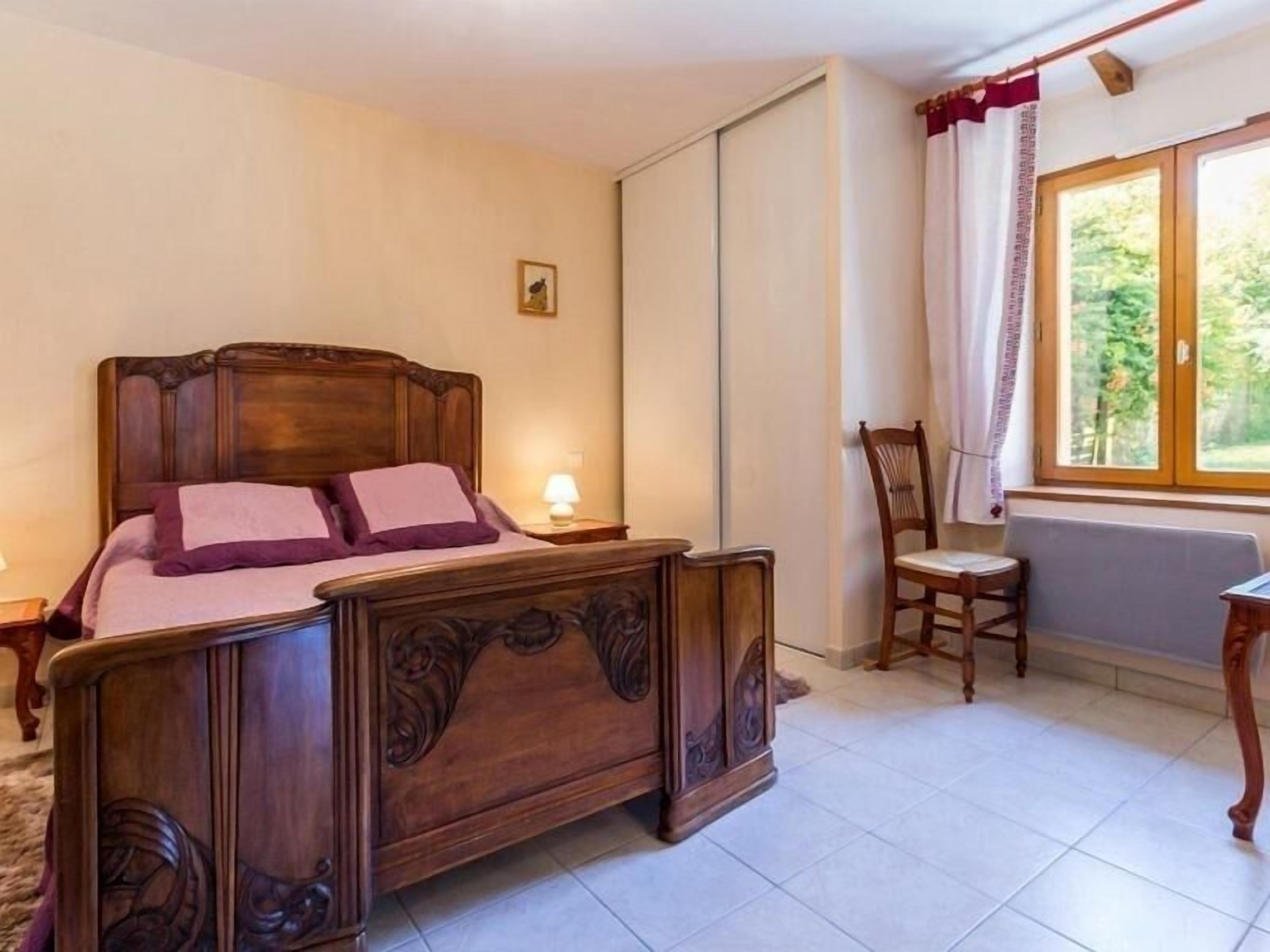 Una camera da letto con un letto di legno, una sedia, un tavolo e una finestra con tende.