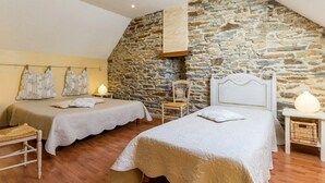 A bedroom with two beds, a stone wall, wooden flooring, and a sloped ceiling.