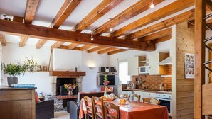 A rustic kitchen with exposed wooden beams, a stone fireplace, and a dining area with a table set for four.