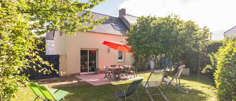 A house with a patio, a table with chairs, and a red umbrella.