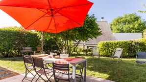 An outdoor patio with a table and chairs, a red umbrella, and a grill.