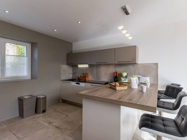 A modern kitchen with grey cabinets, a wooden countertop, and a built-in island with bar stools. - Family-Friendly Farmhouse: 4 km to Beach, 2 km to Shops, Garden, WiFi, Baby Gear (Pornic)