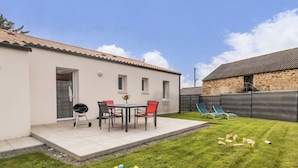 A patio area with a table and chairs, a small garden with colorful balls, and a stone building in the background.