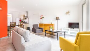 A modern living room with a sofa, armchair, and coffee table. There is a TV and a cabinet with a vase of flowers.