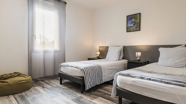 A modern bedroom with two beds, a bean bag, and a large window.