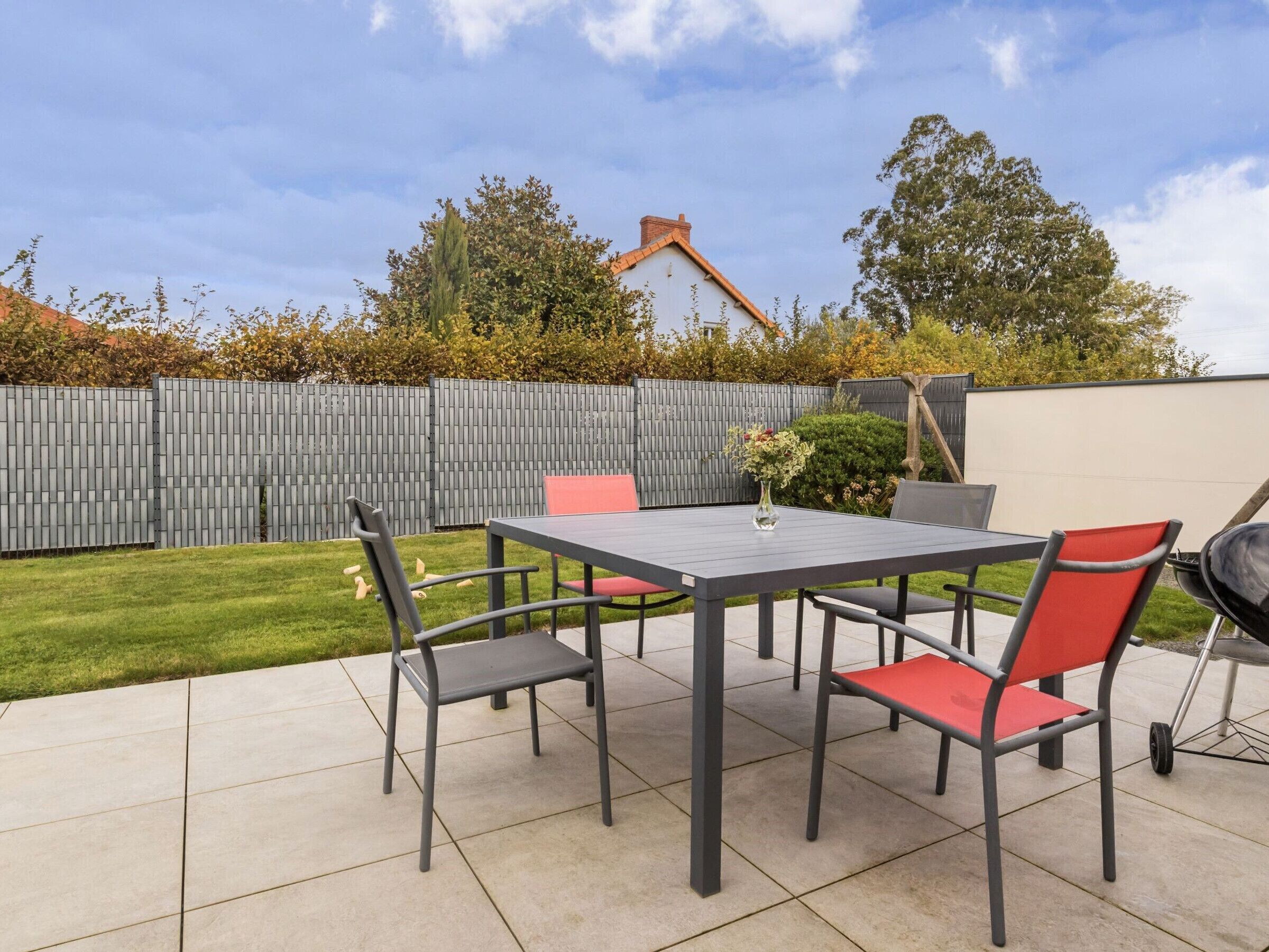 A patio with a table and chairs, a grill, and a wooden fence.