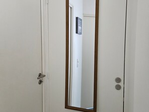 Eine geschlossene Tür mit Holzrahmen und einem Metallgriff, ein Spiegel der einen Türgriff und ein Schild an der Wand reflektiert.