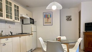 A kitchen with white cabinets, a glass table, and white chairs. There is a microwave, a stove, and a ceiling light fixture. - Waterfront 2-Bedroom Cottage with Terrace in Saint-Michel-Chef-Chef (Saint-Michel-Chef-Chef)