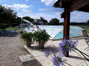 Un espace extérieur abrité comprenant une piscine, des sièges et des plantes en pot.