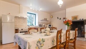 Un comedor con una mesa preparada para cuatro personas, rodeada de sillas de madera. Se ve una cocina con electrodomésticos blancos y un salpicadero de azulejos al fondo.